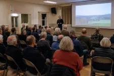 Samrådsmöte i en bygdegård med åhörare som lyssnar på en presentatör